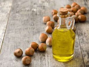 Jug of hazelnut oil on a table with a pile of hazelnuts